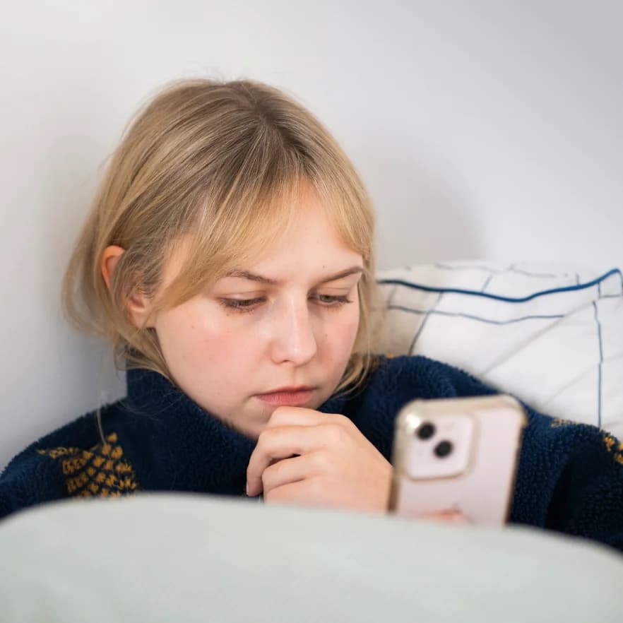 Kobieta leżąca w łóżku, patrząca w ekran telefonu